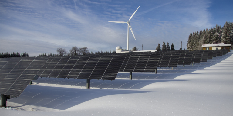 Parque fotovoltaico cubiero de nieve y al fondo un aerogenerador.