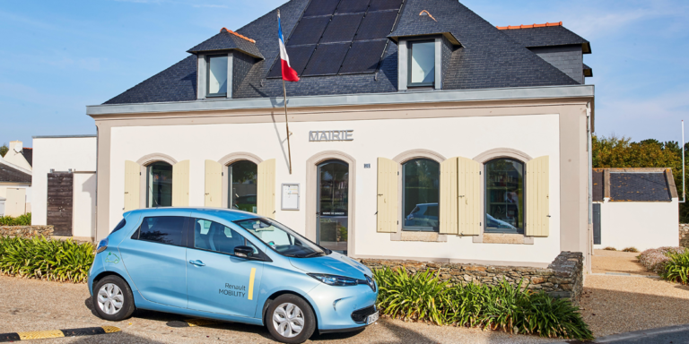 Vehículo eléctrico de Renault aparcado junto a un edificio público con paneles fotovoltaicos sobre su cubierta.