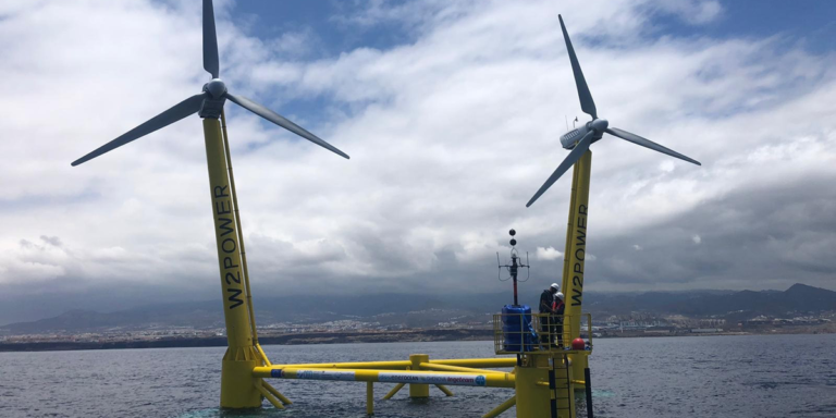 Plataforma eólica marina con dos turbinas frente a la costa de Gran Canaria con dos operarios trabajando en su puesta en funcionamiento.