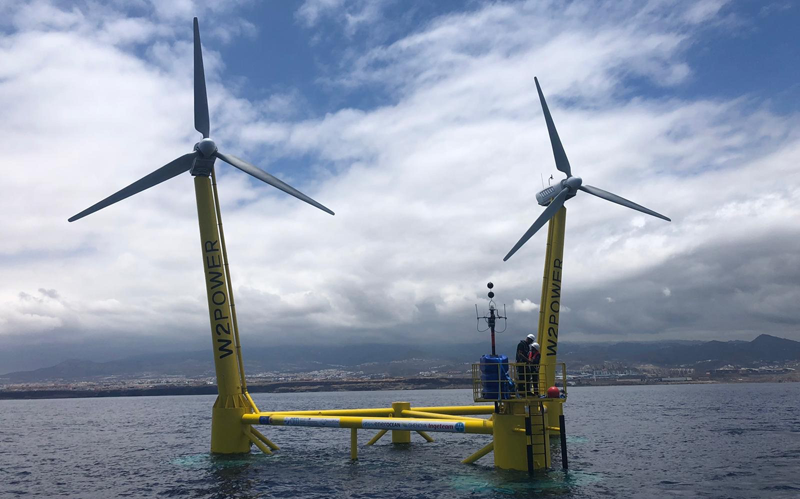 Plataforma flotante eólica con dos turbinas frente a la costa de Gran Canaria con dos operarios trabajando en su puesta en funcionamiento.